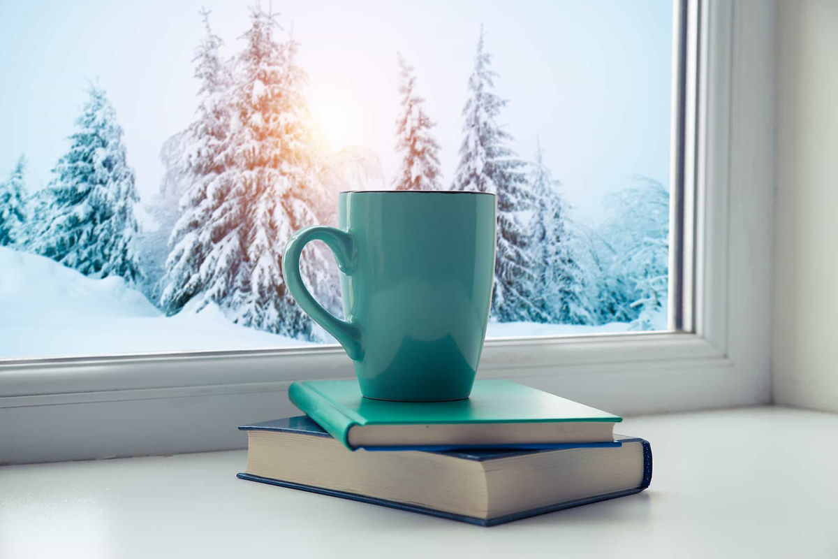 Photo of cup on top of books in front of a window in the winter